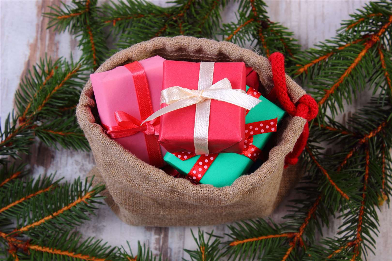 Wrapped colorful gifts for Christmas, birthday or other celebration in jute bag and spruce branches on old wooden white table